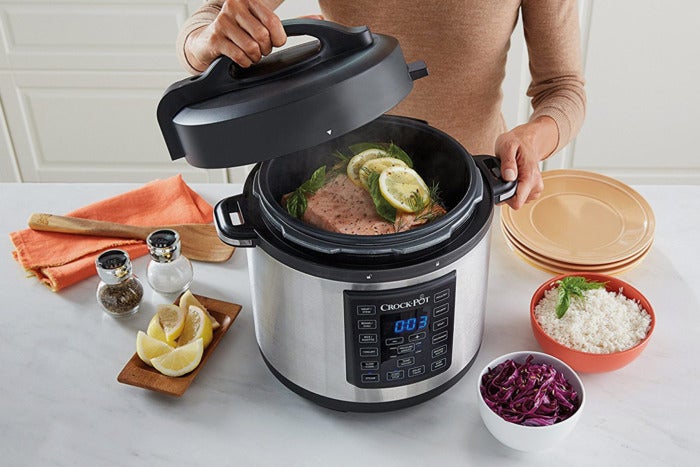 Woman opening a Crockpot to show fish cooking inside.